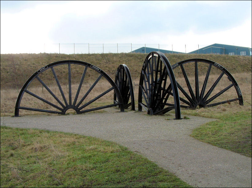 Four pithead winding wheels, half set into the ground. Pointing in four different directions