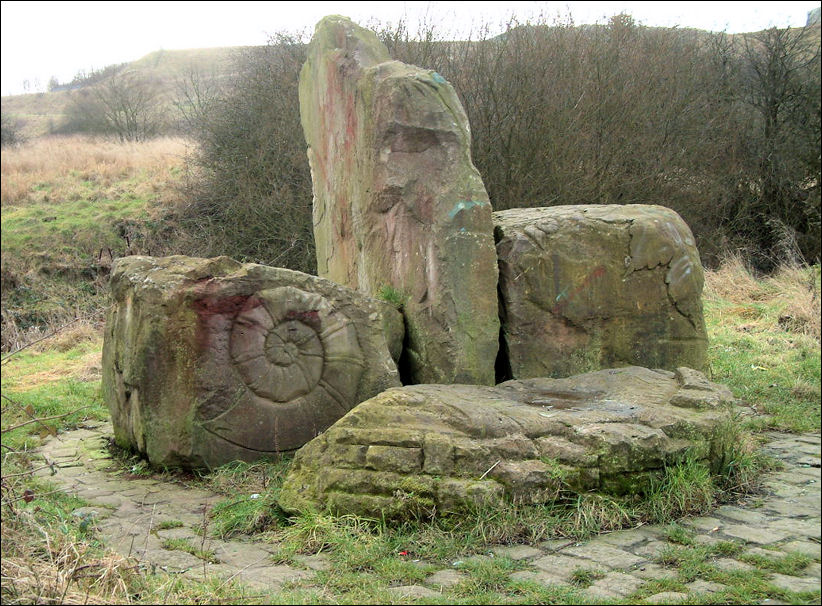 The Stone Gateway to Berryhill Fields - three large boulders appear behind a smaller, lower stone block whose sides are carved to suggest a stone wall