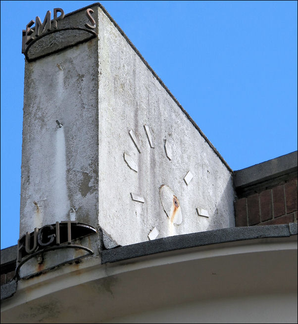 remains of a concrete clock, it has a face once each side and the words Tempus Fugit in wrought iron work