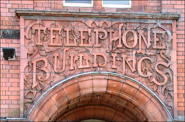Doorway to right with terracotta scroll and lettering over given name, "Telephone Buildings"
